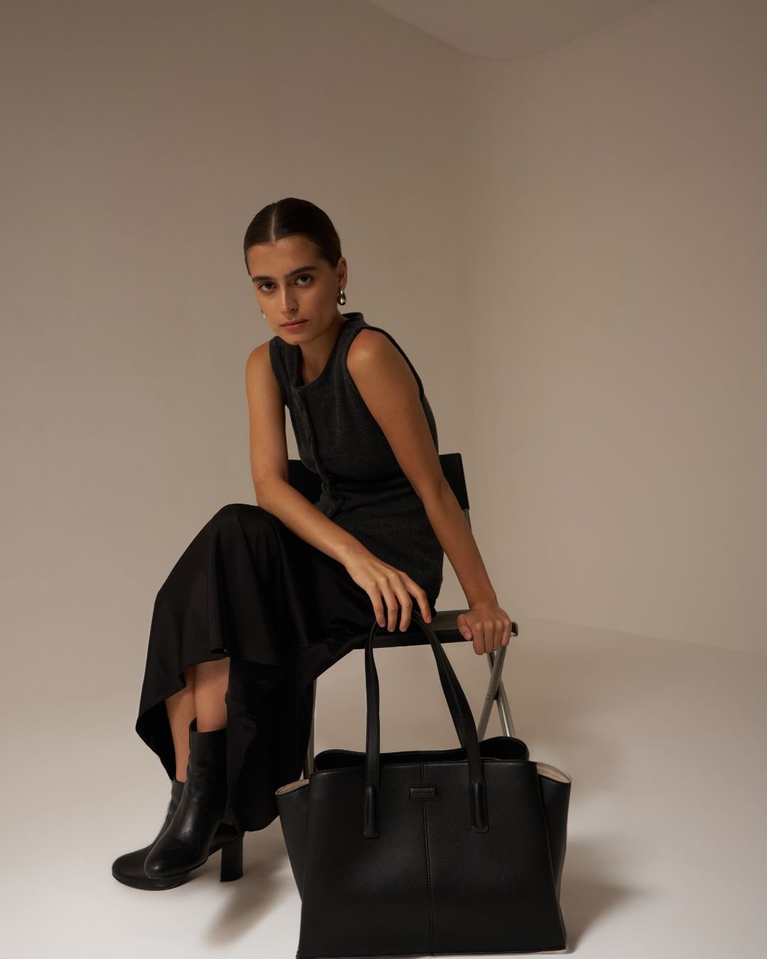 Black tote bag held by model, featuring two top handles and clean structured silhouette.