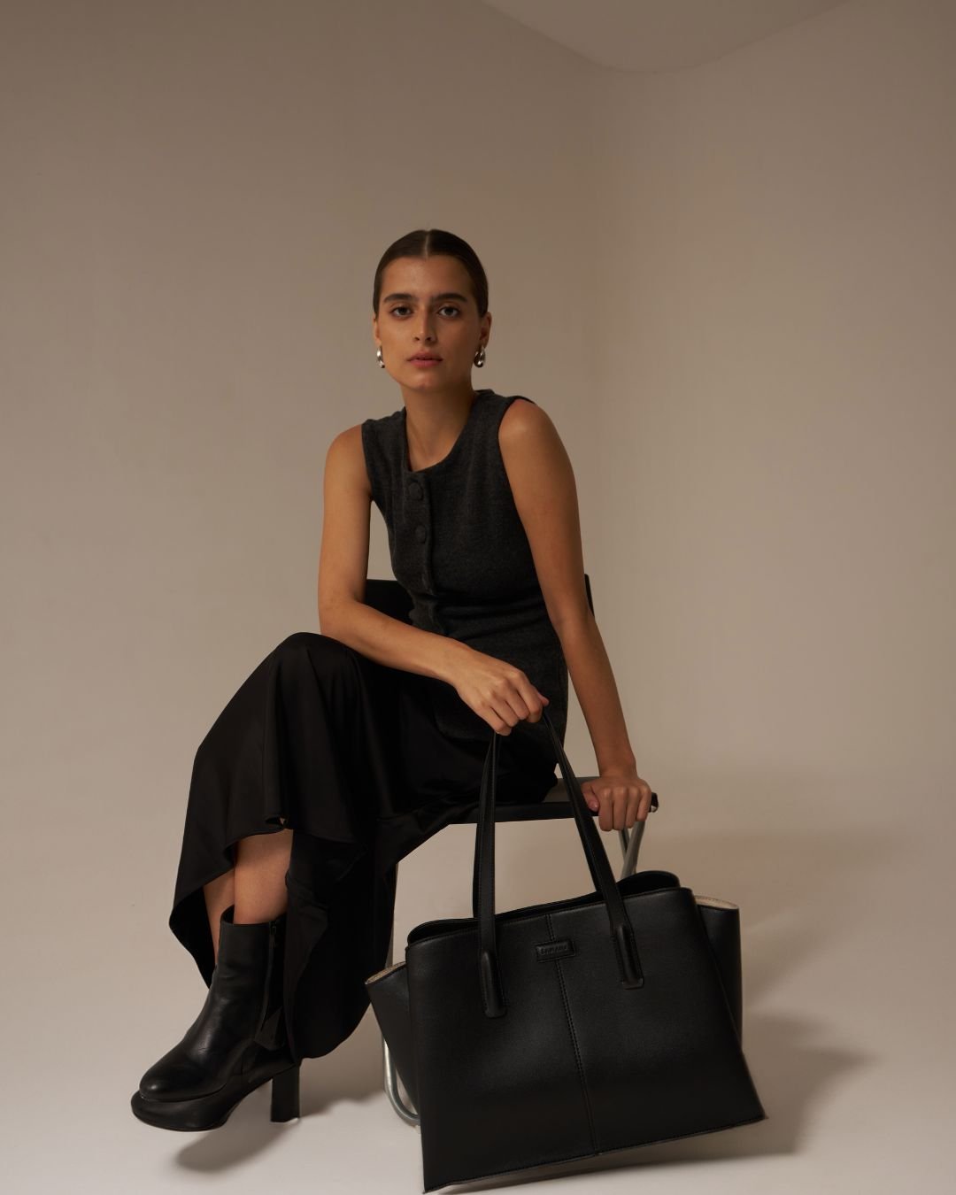 Black tote bag with two top handles, front logo plaque, styled with minimal hardware.