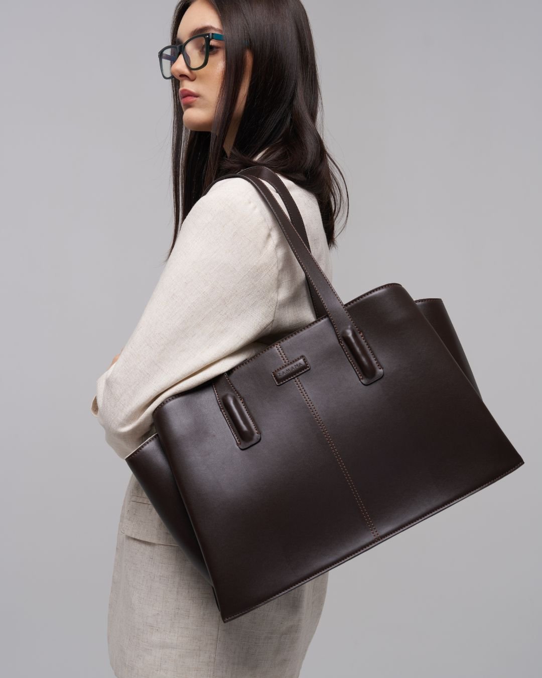 Dark brown leather tote bag side view with front stitched trim and top handles