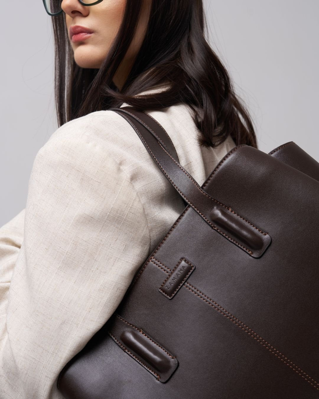 Dark brown leather tote bag close-up: front straps and stitched panel details