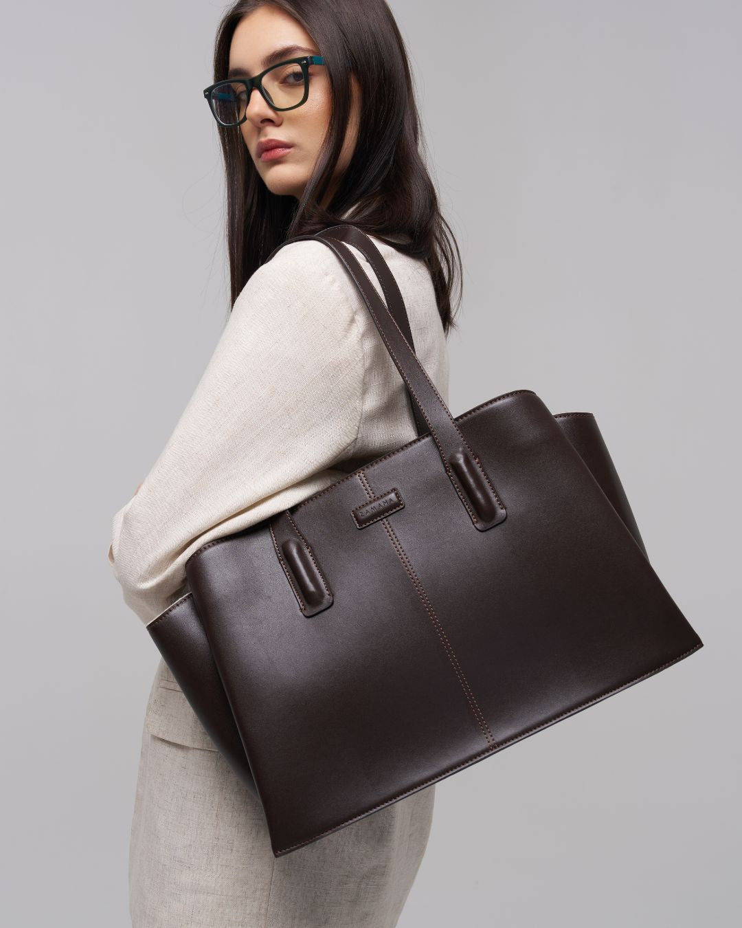 Dark brown leather tote bag with shoulder strap and front pocket-style stitching