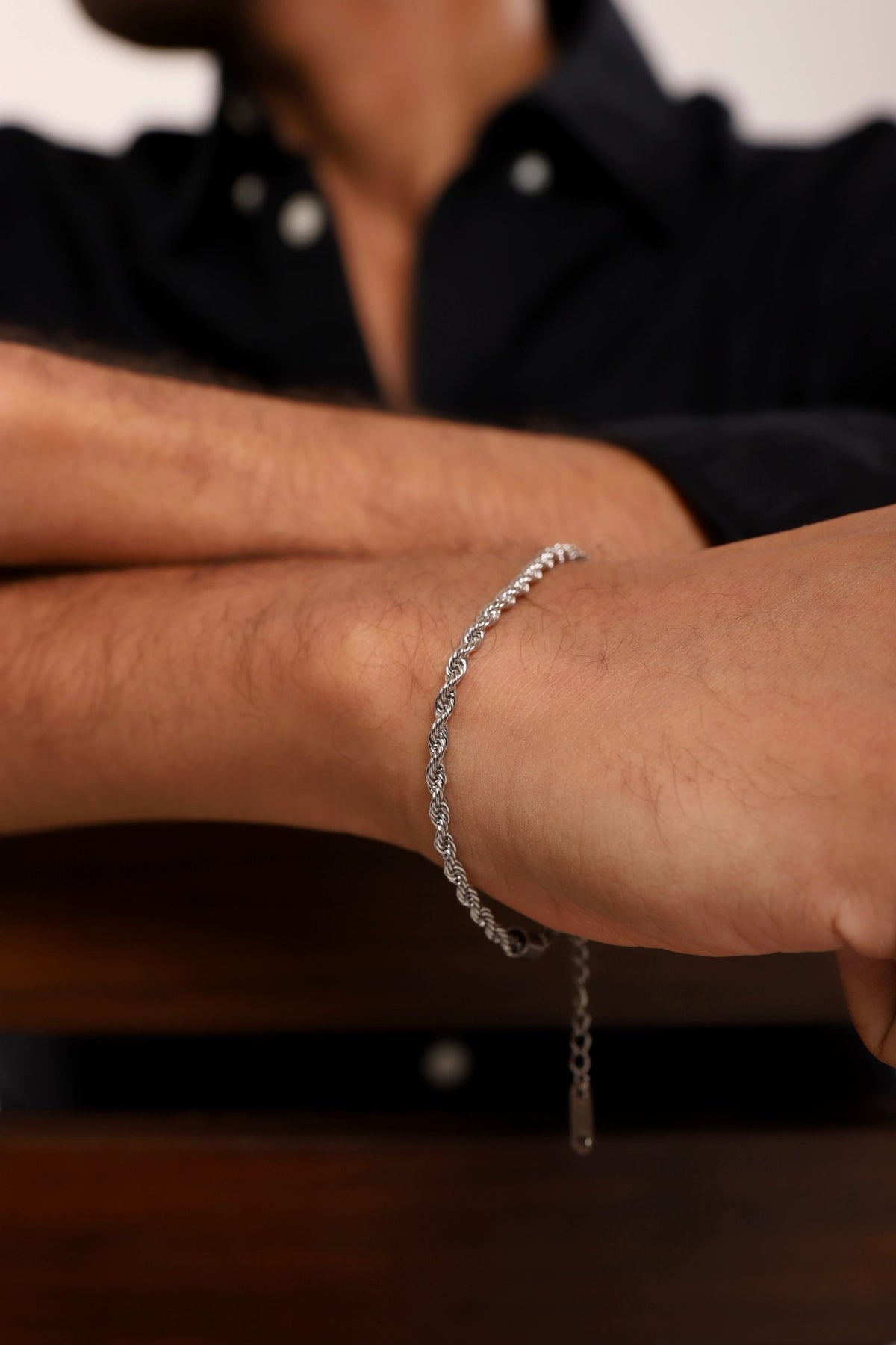 Silver rope chain bracelet on wrist, showing chain links and dangling charm