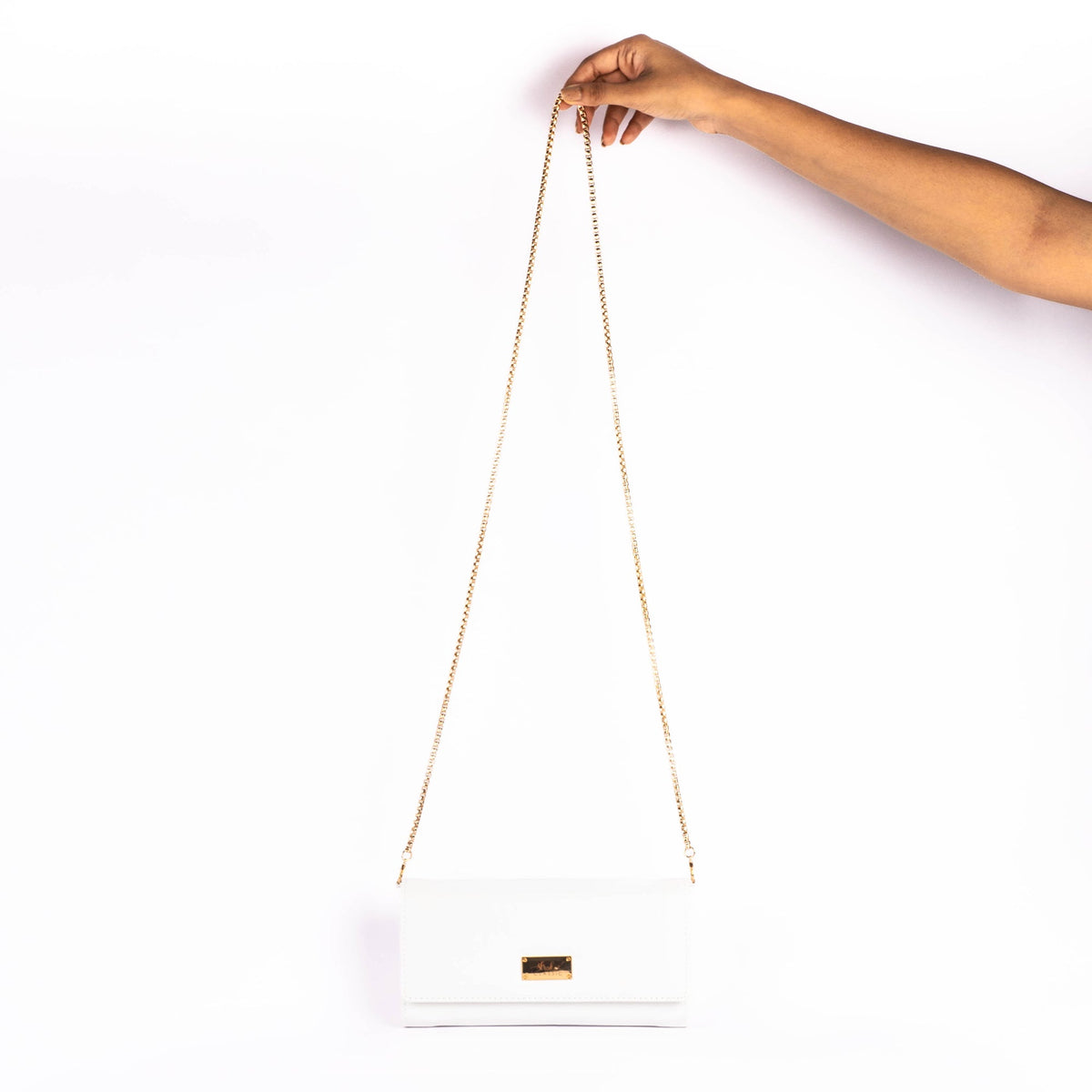 White small clutch wallet with gold chain sling, held for shoulder carry