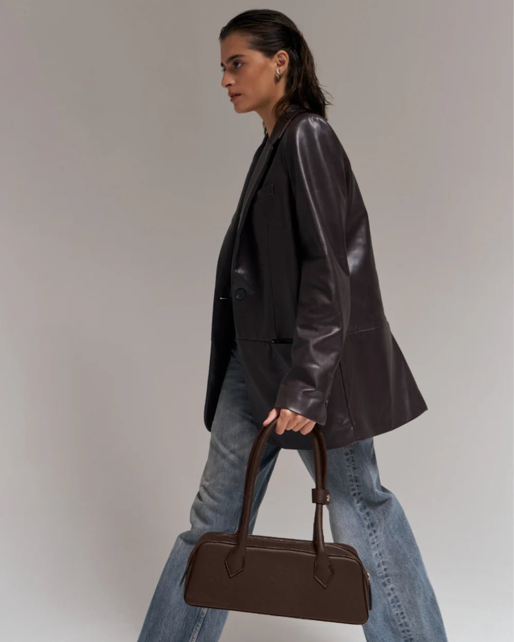 Dark brown baguette handbag with two top handles, carried at side