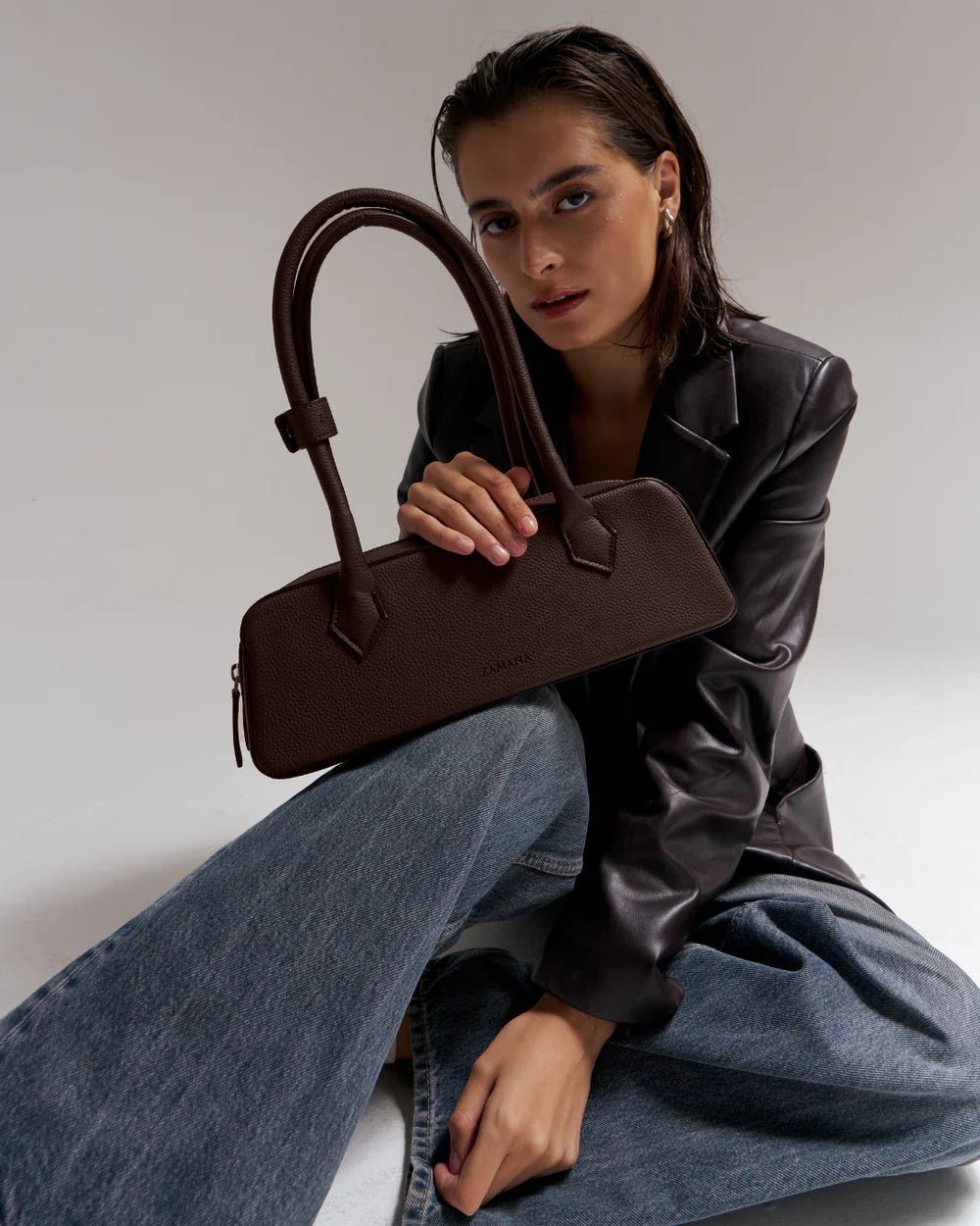 Dark brown handbag with two top handles, held by the model