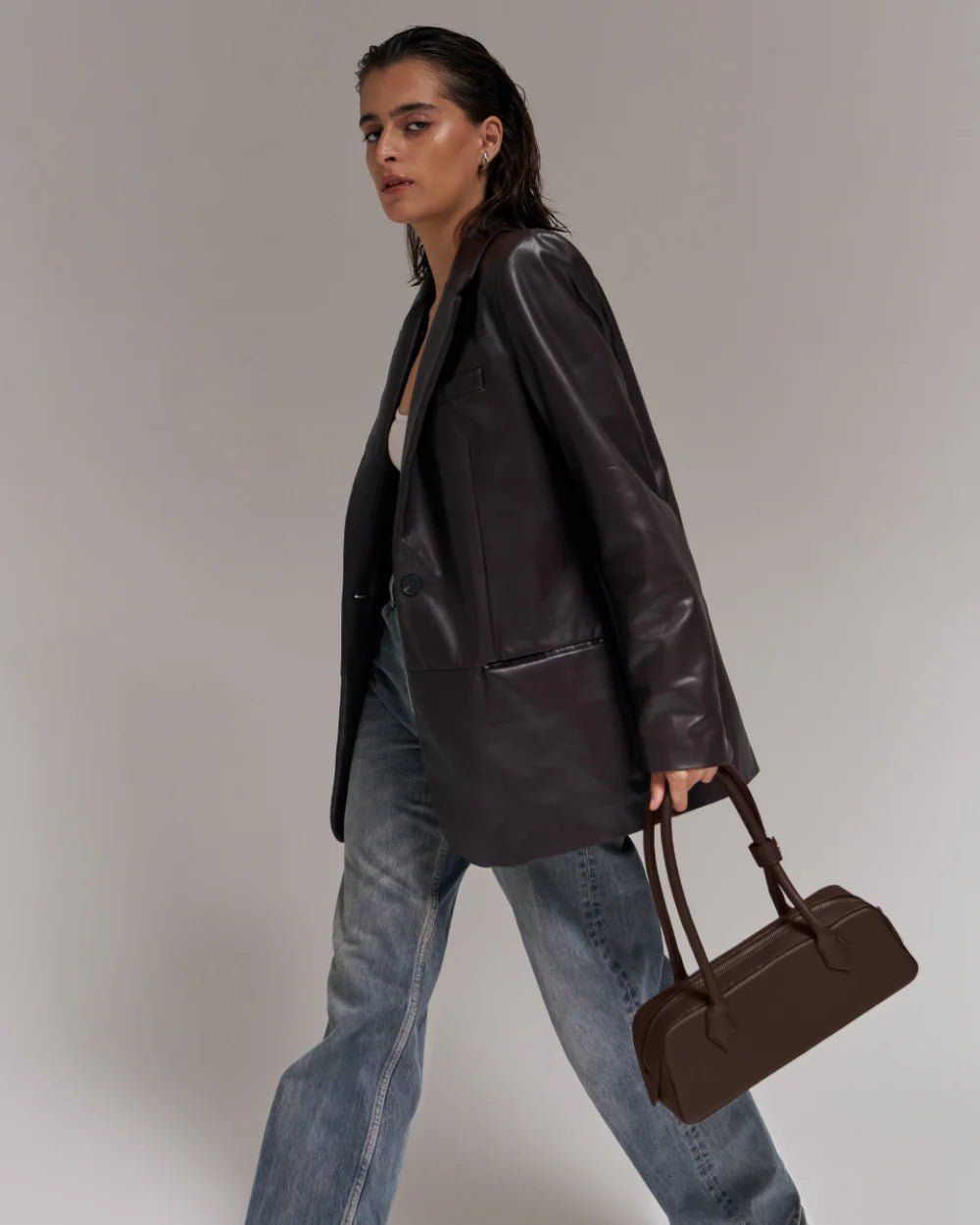 Dark brown handbag with two top handles, held close while walking