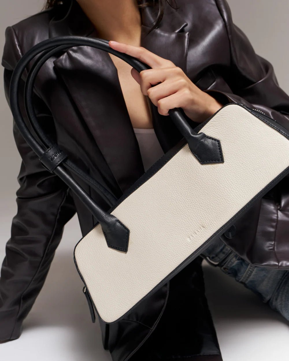 White baguette handbag with black top handles and strap detail, held in hand