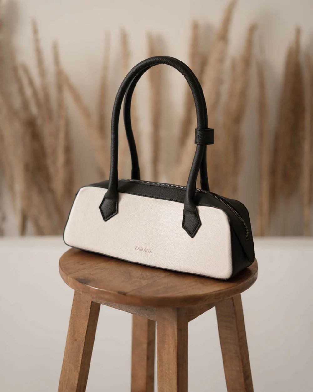 White baguette handbag with black top handles and small brand mark on front