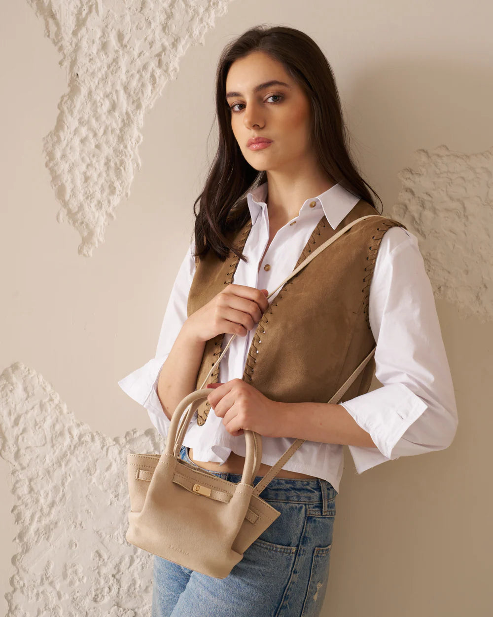 Cream tote bag with top handles and front strap buckle, held at chest
