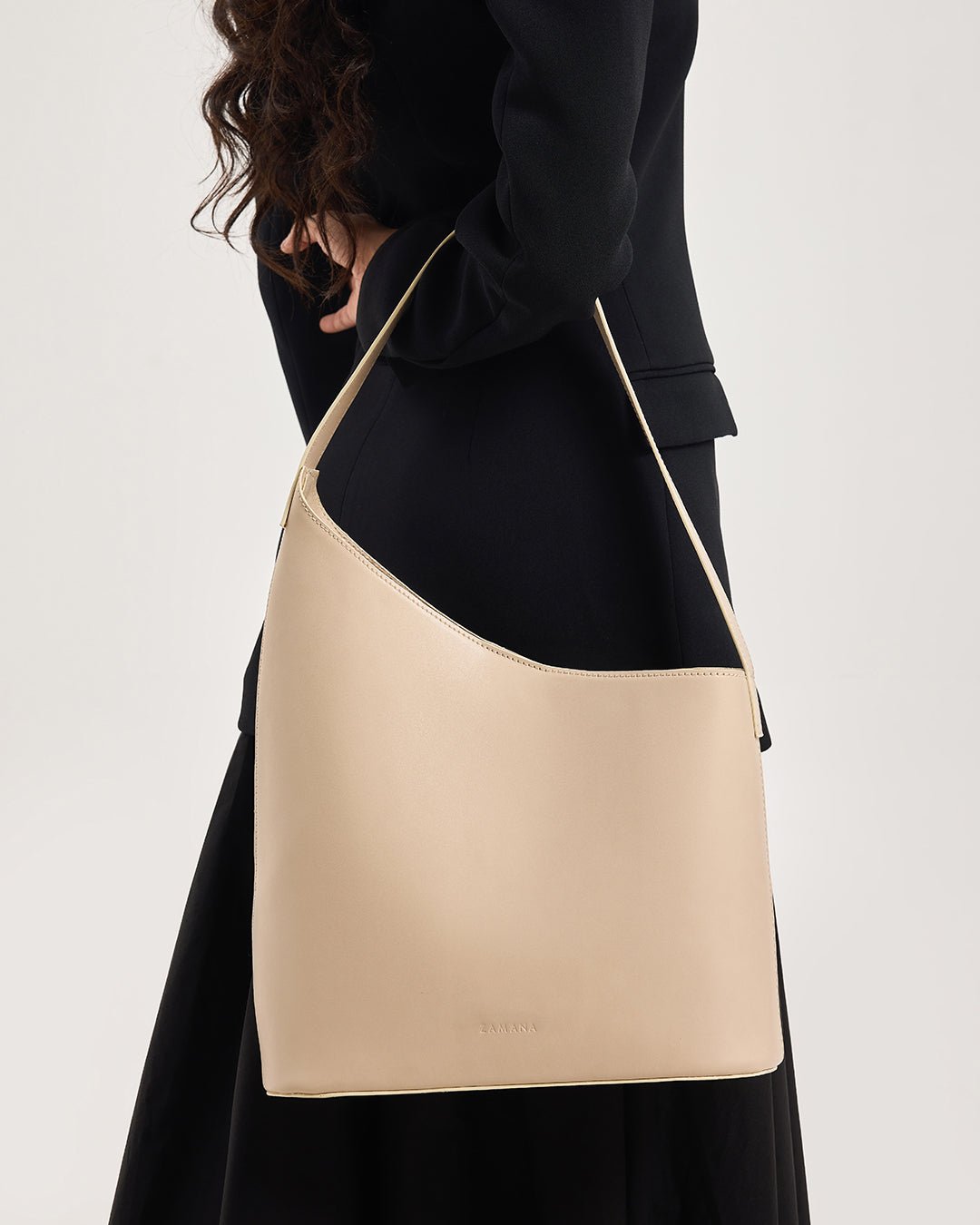 Beige hobo tote bag on shoulder with long handle, model in black outfit