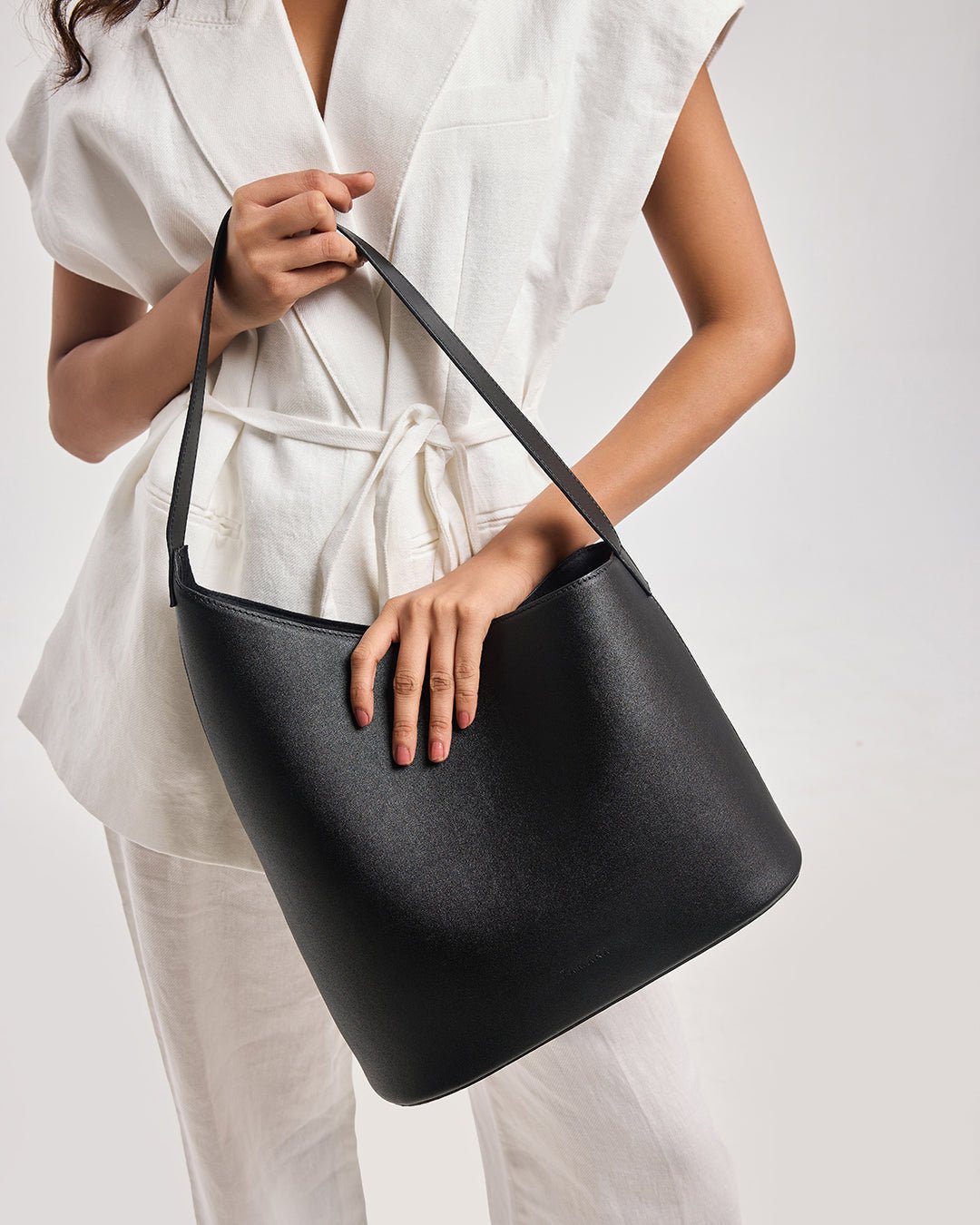 Black bucket shoulder bag with open top and wide strap, carried by model