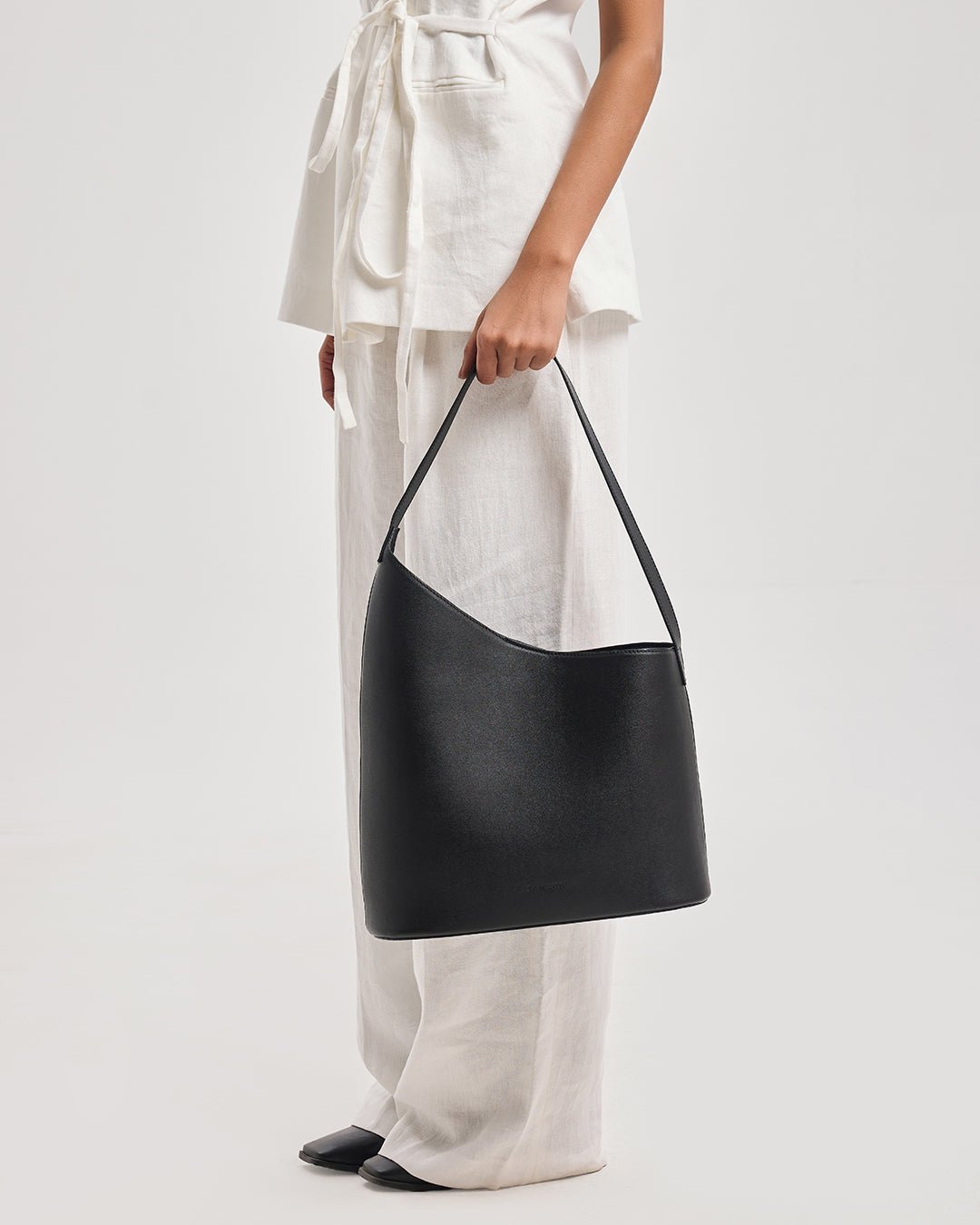 Black bucket shoulder bag with structured body and open top, side profile