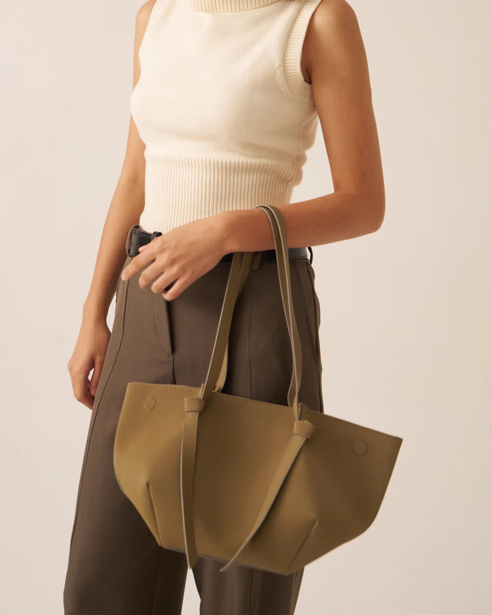 Olive tote bag with front pocket and strap hardware, close-up styled on model