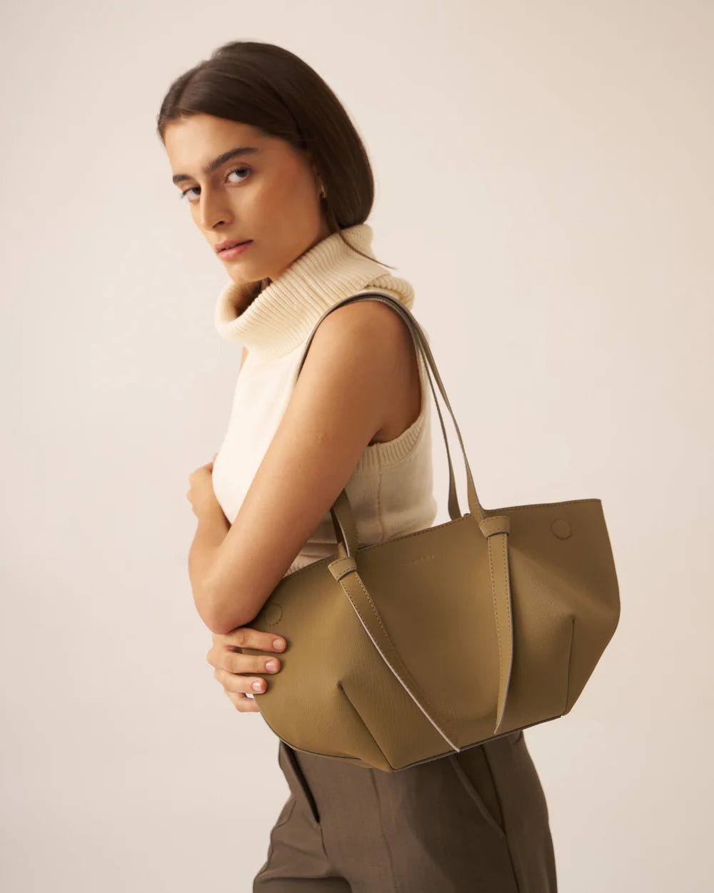 Olive tote bag with dual handles and side seams, worn by model in profile