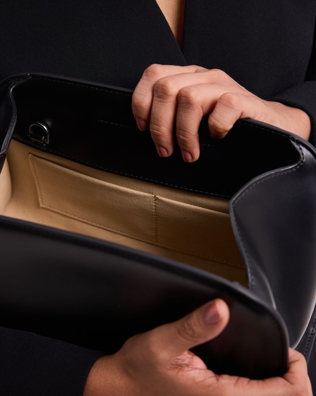 Black leather tote-style bag open to show beige interior lining and top frame edge.