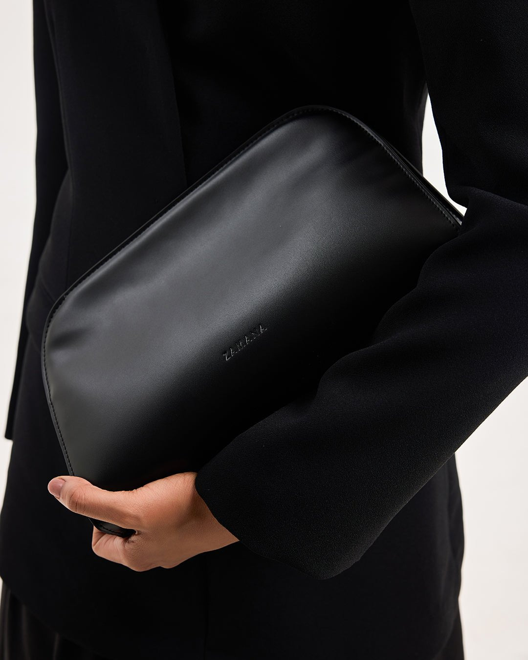Black leather bag with curved top opening, held across the arm; front logo visible.