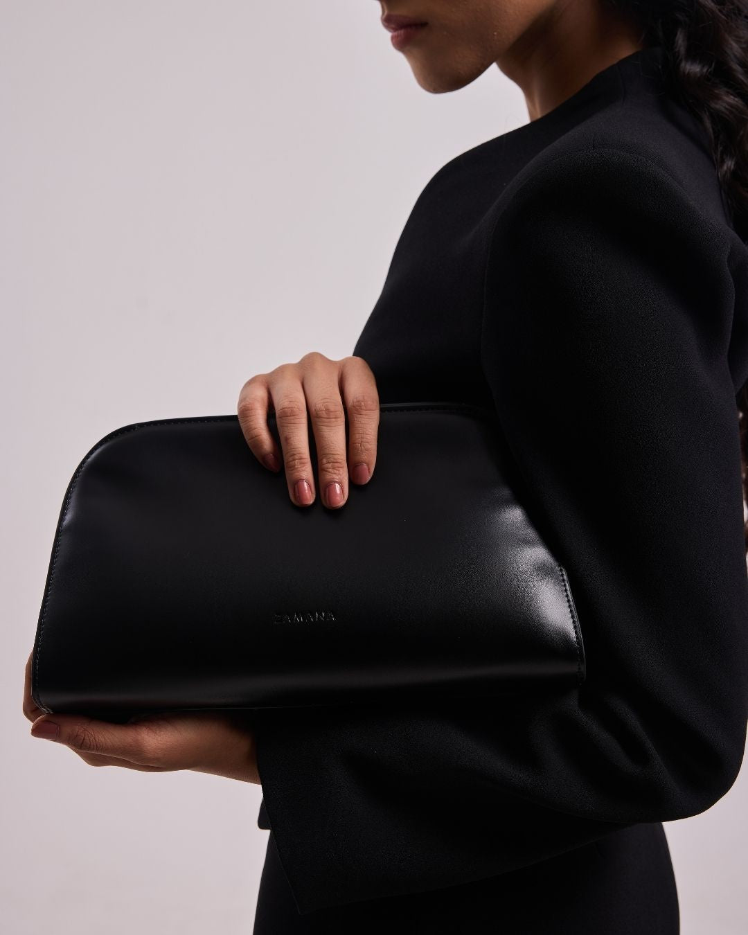Black leather top-handle bag held by the side of the body with stitched details.