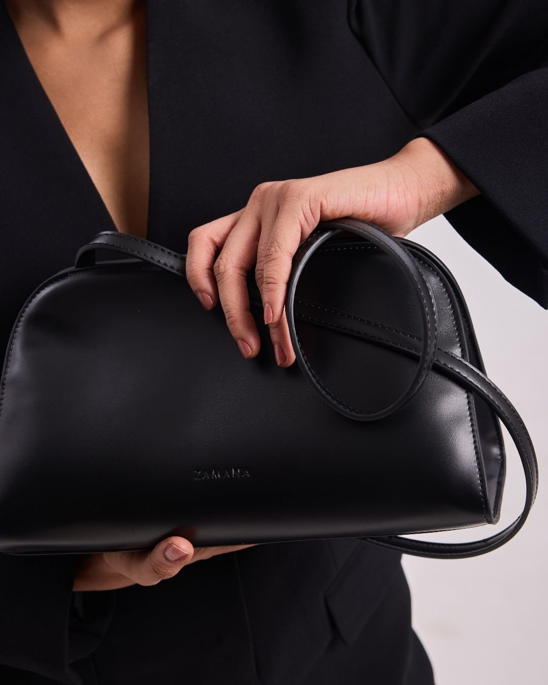 Black leather top-handle bag with a rounded strap handle and subtle front logo.