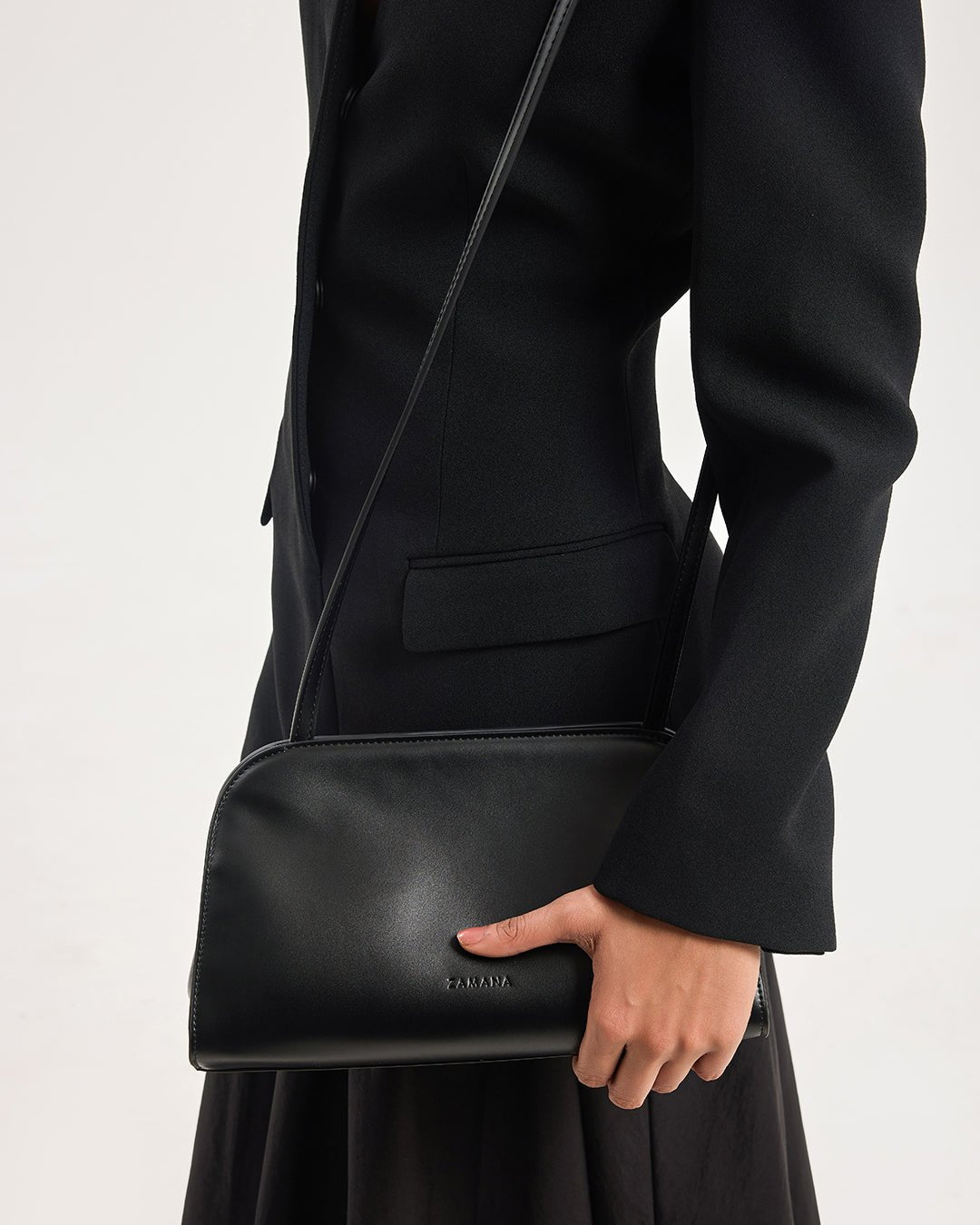 Black leather crossbody bag with long strap and front flap-like panel detail.