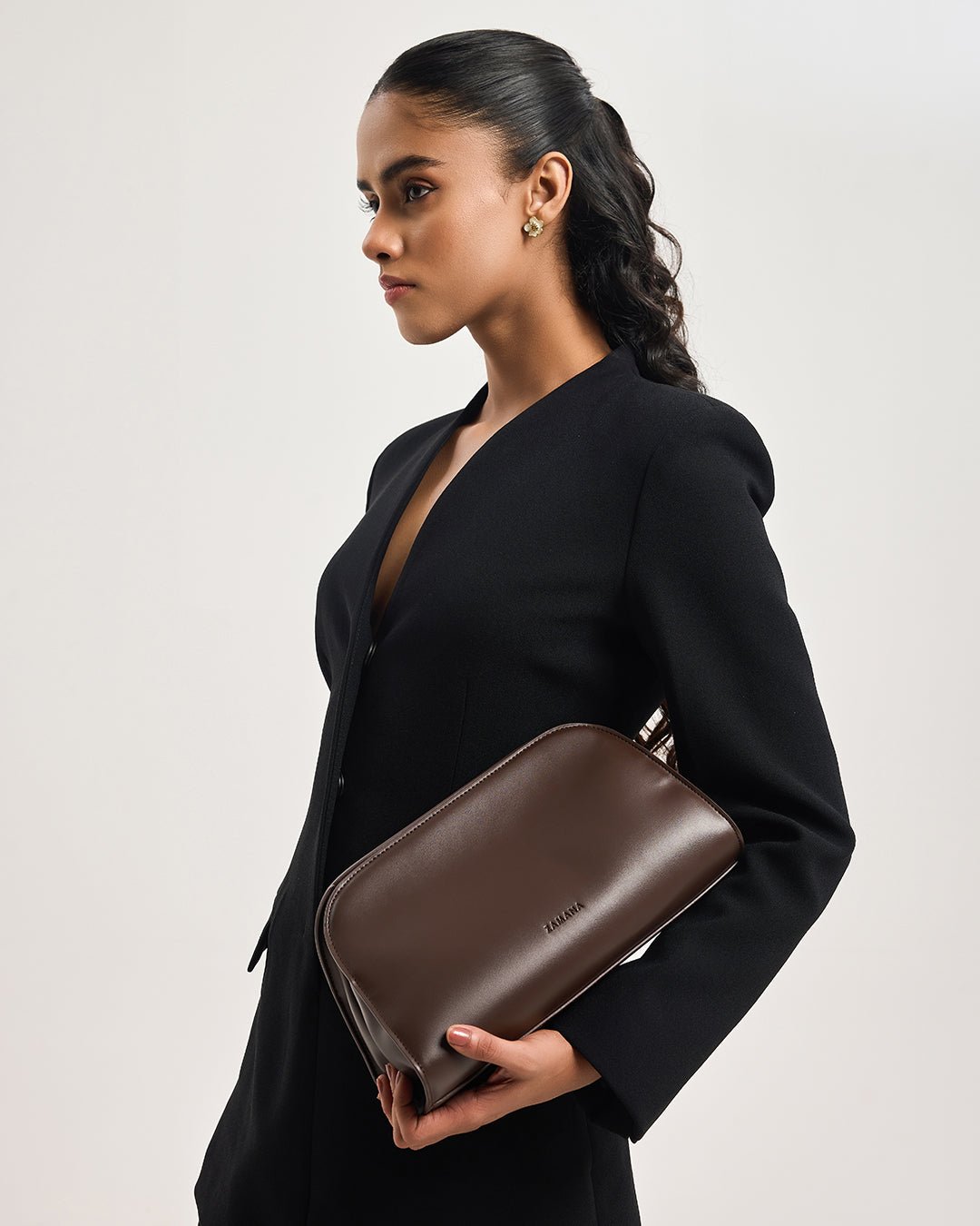 Dark brown leather clutch with side profile, worn with long strap across model’s front
