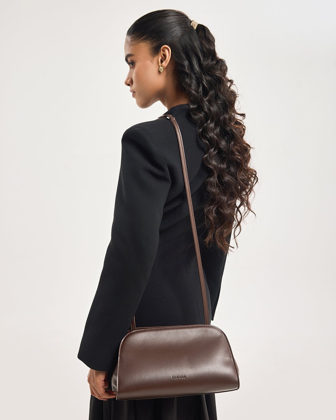 Dark brown leather crossbody clutch with long strap, model shown from back