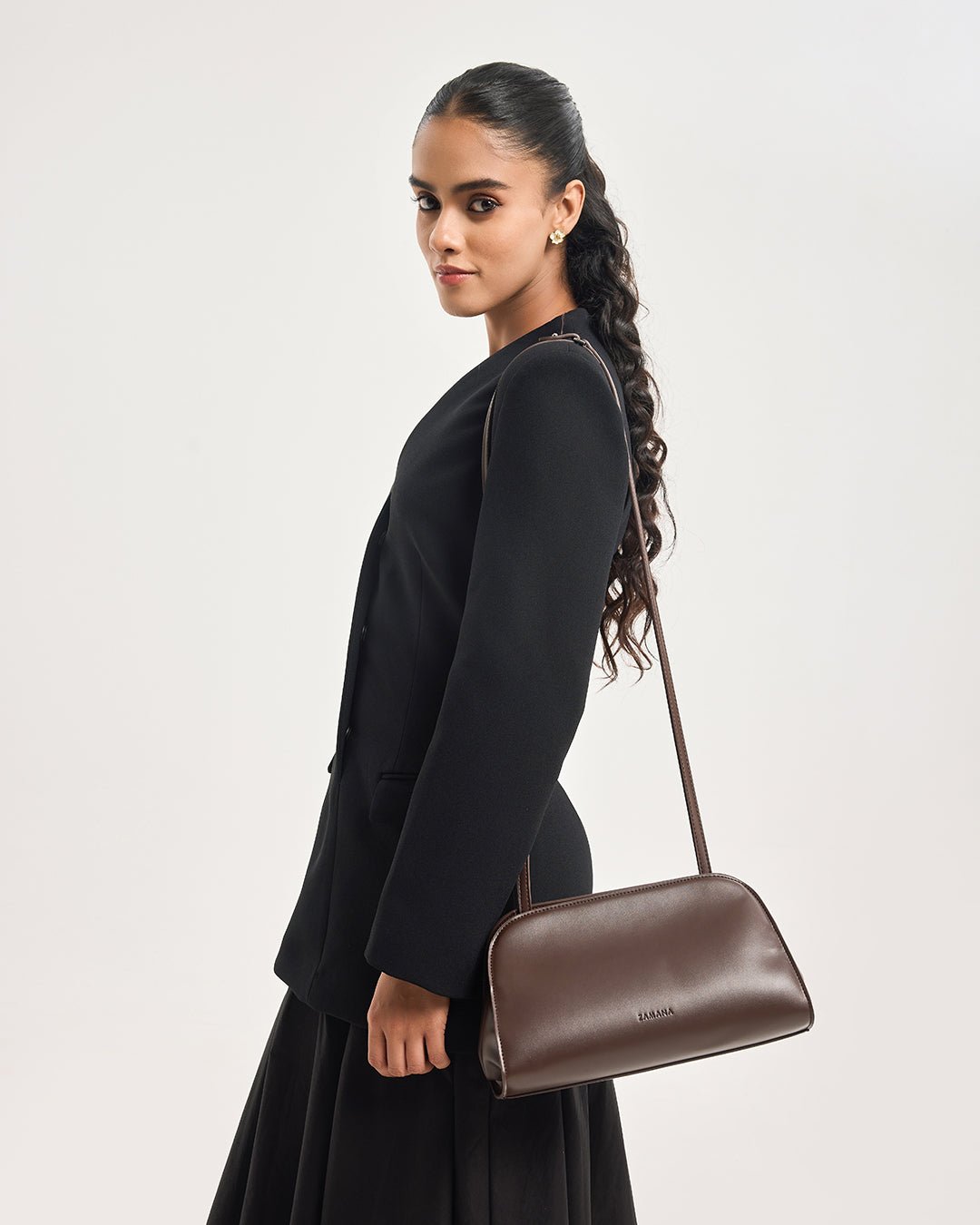Dark brown leather crossbody clutch bag with long shoulder strap, side view on model
