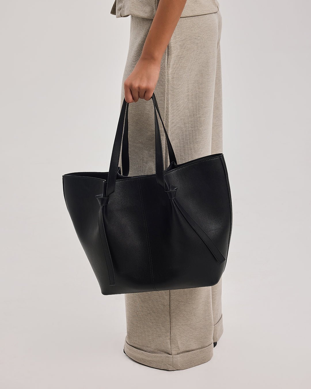 Black leather tote bag held by top handles with side tie accents