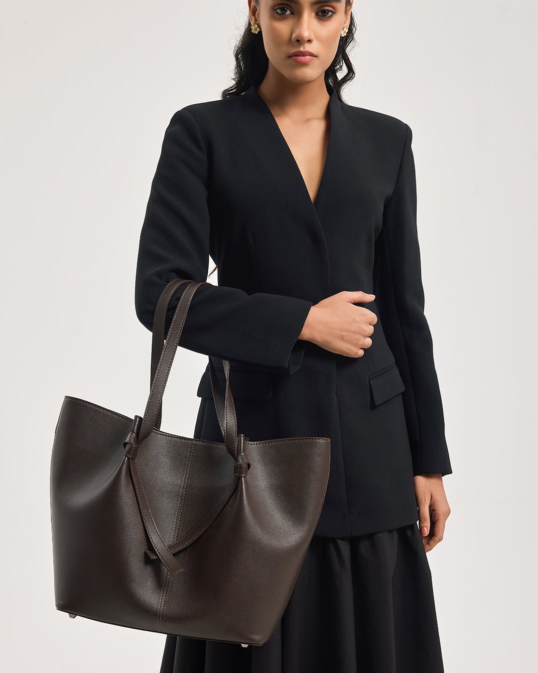 Dark brown tote bag with two handles and V-shaped front strap detail.