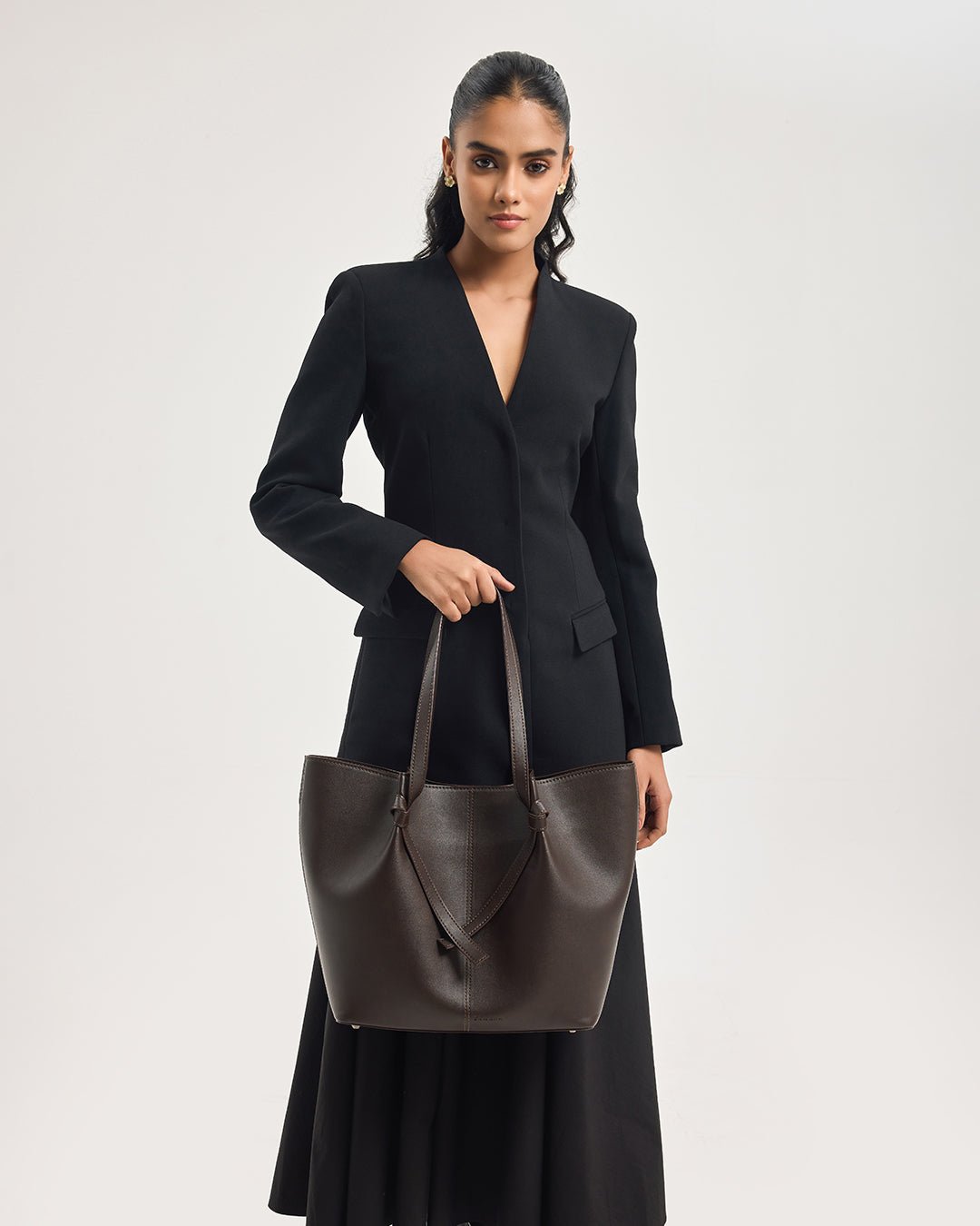 Dark brown leather tote bag with two handles and V-shaped front strap detail.