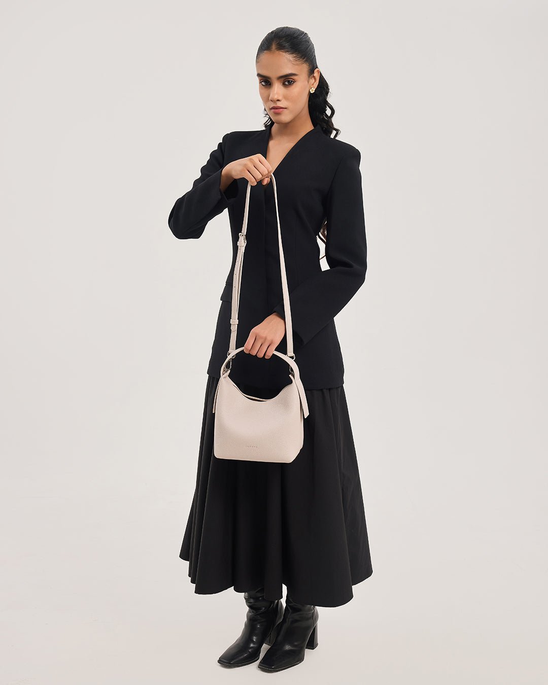 Cream hobo crossbody bag worn with adjustable strap and curved top handle