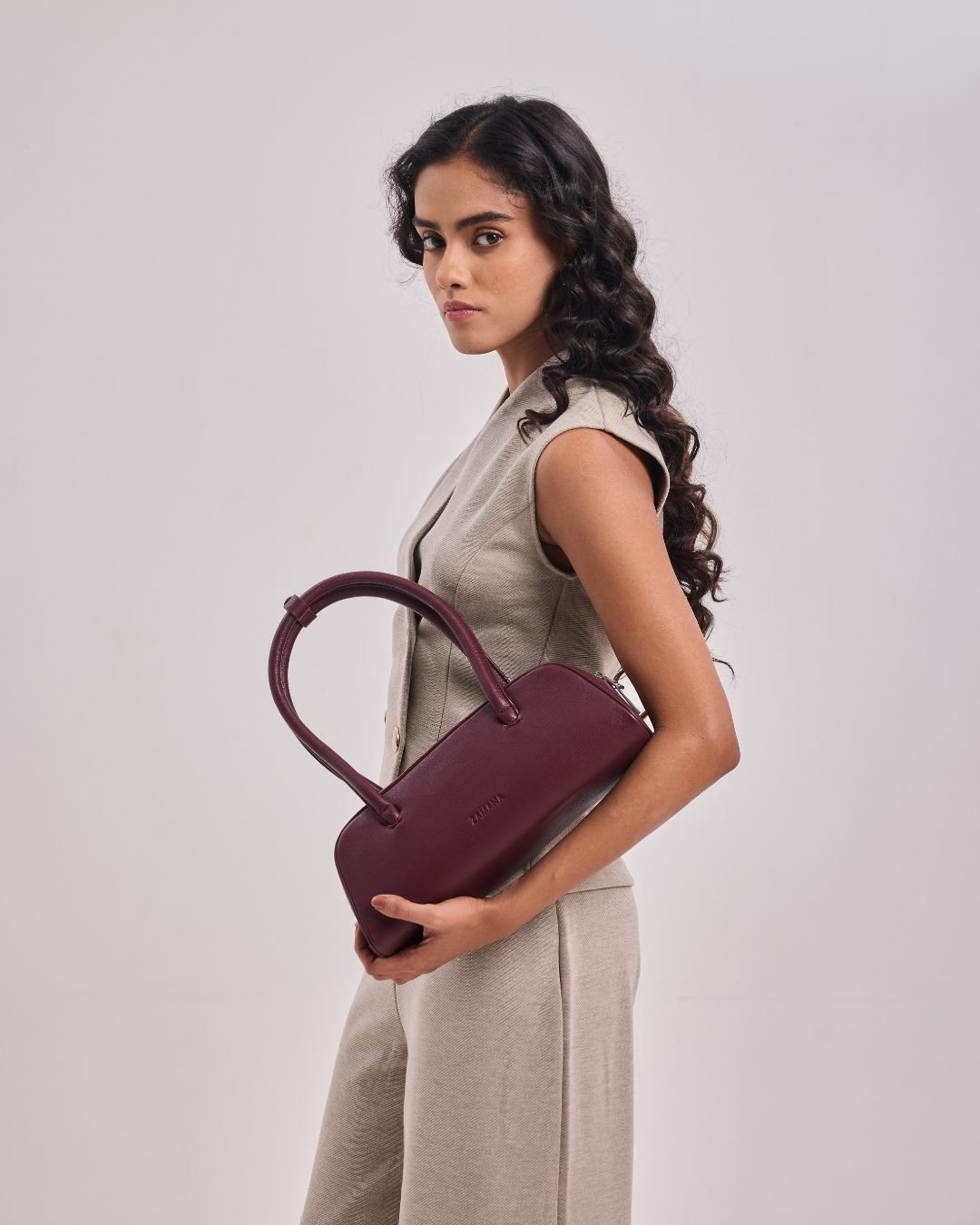 Burgundy mini satchel handbag held in hand, with short top handles.