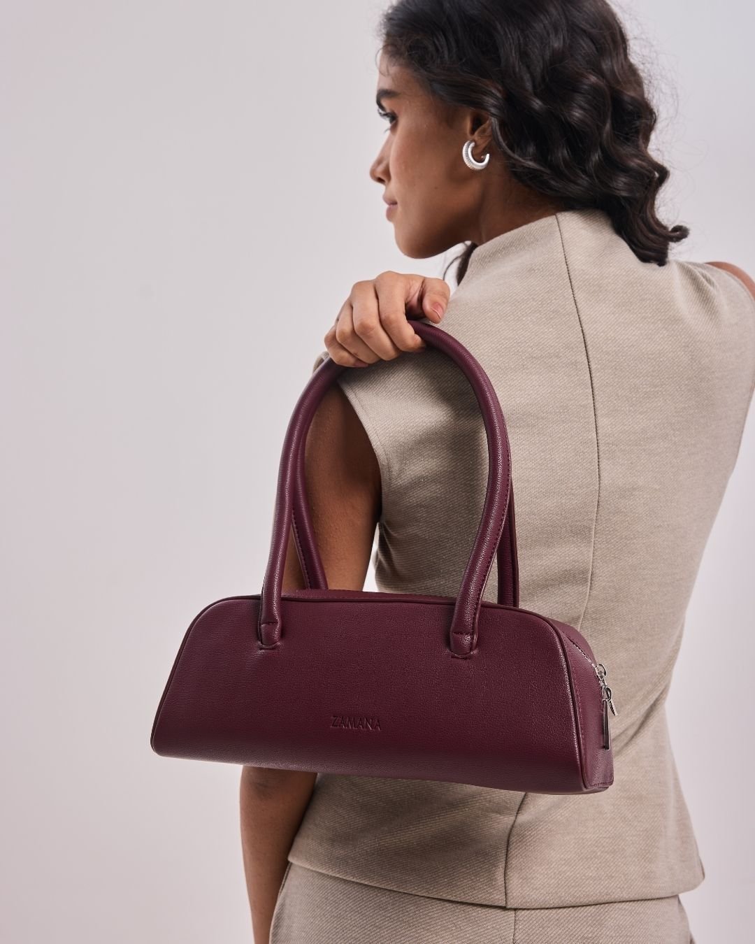 Burgundy mini satchel handbag with two top handles and curved silhouette.