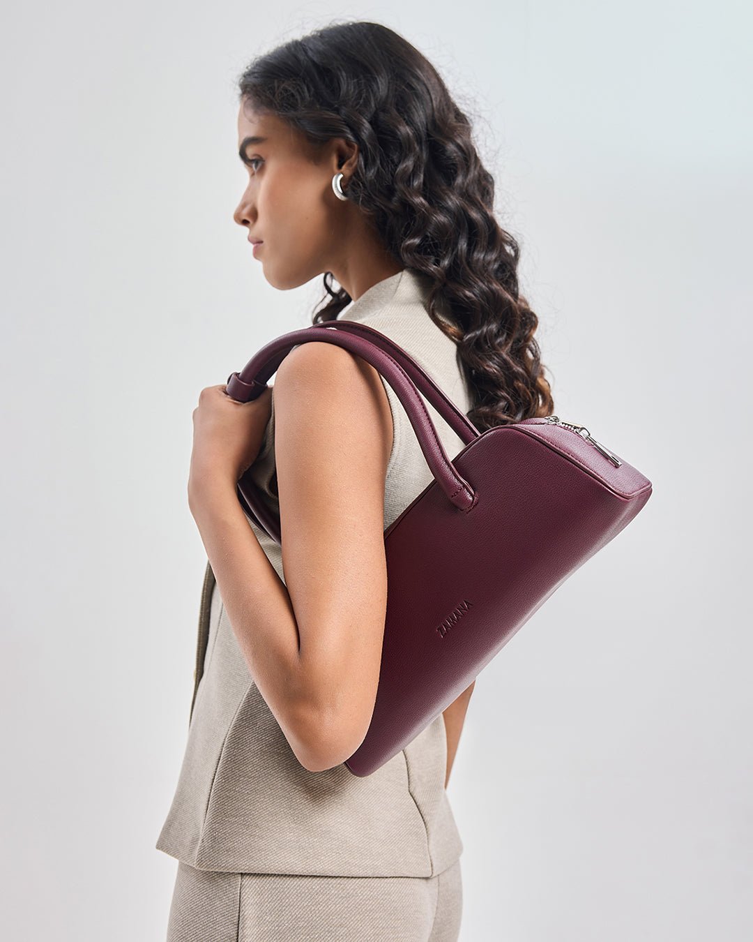 Burgundy tote handbag with rounded handles and front logo, worn at shoulder