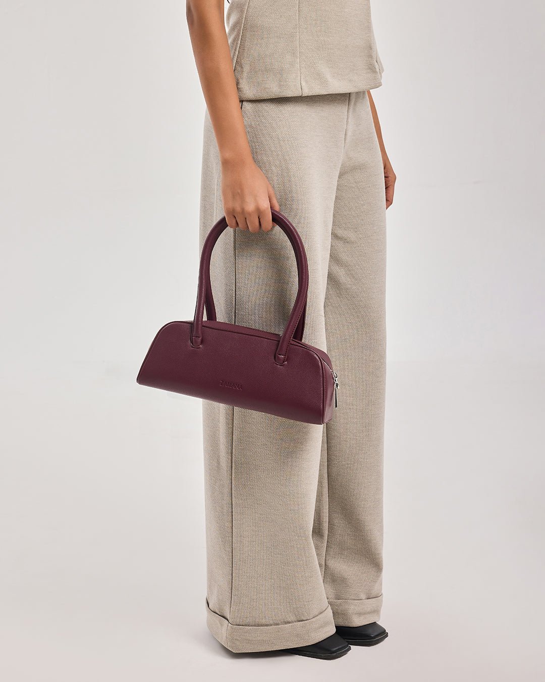 Burgundy mini satchel handbag with top handles, carried at side view.
