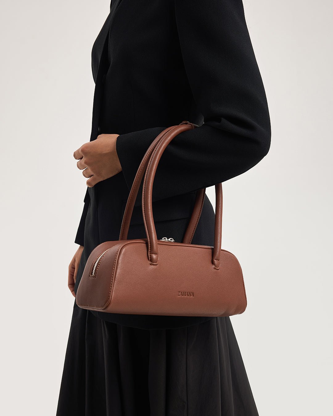 Chocolate brown top-handle handbag with zip detail and short handles in hand