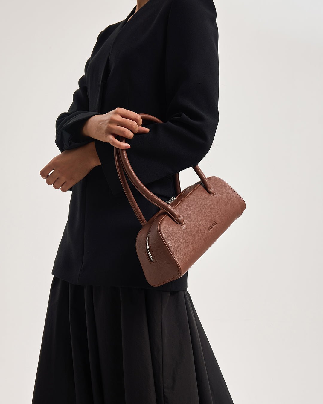 Chocolate brown small top-handle handbag held at side, front logo visible
