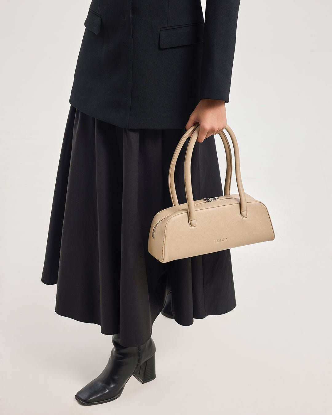 Cream/tan handbag with top handles held by model in a black skirt outfit