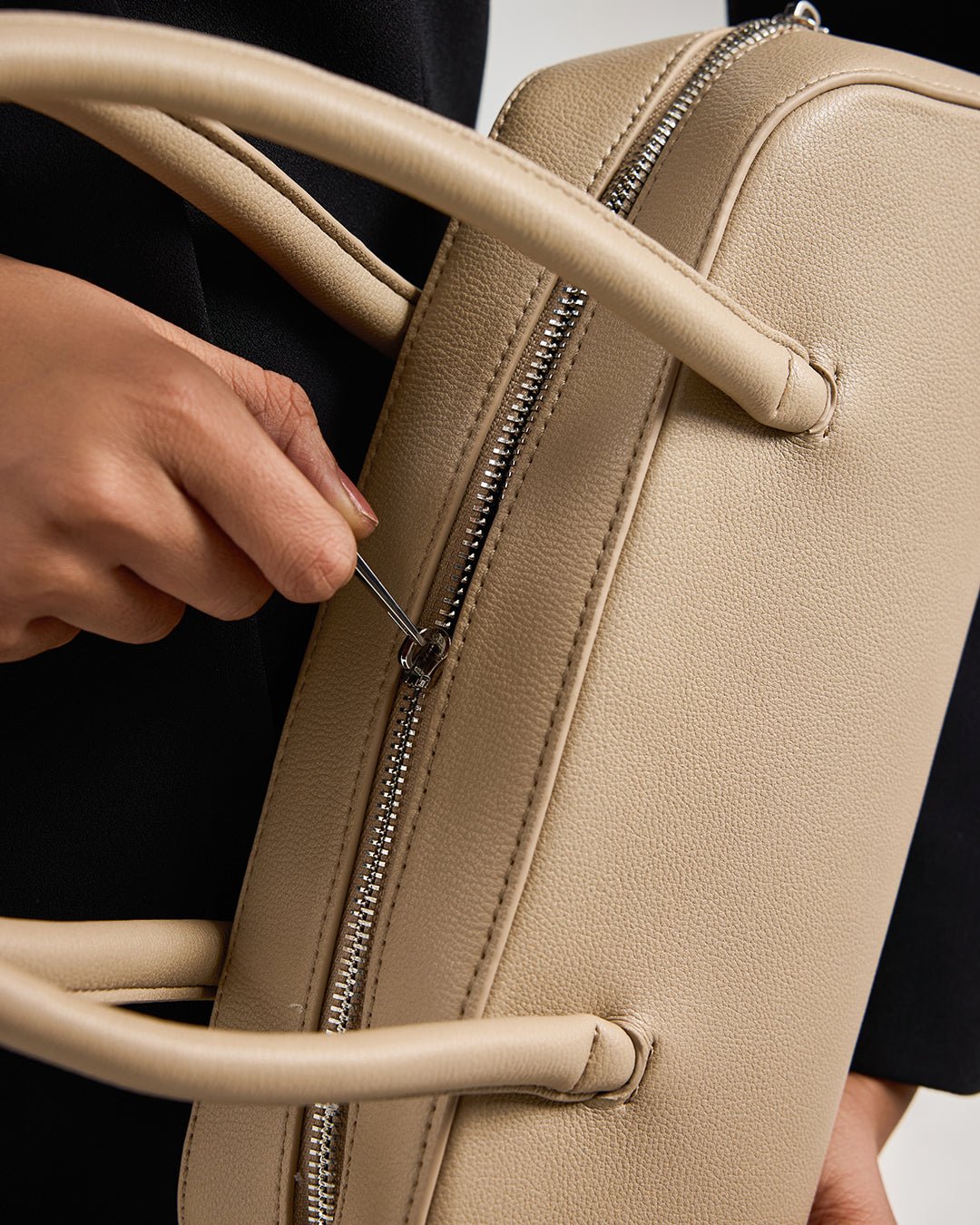 Cream handbag close-up showing front zipper and textured leather-look finish