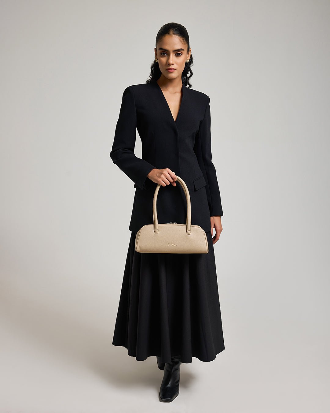 Cream/tan top-handle handbag carried with a black V-neck outfit
