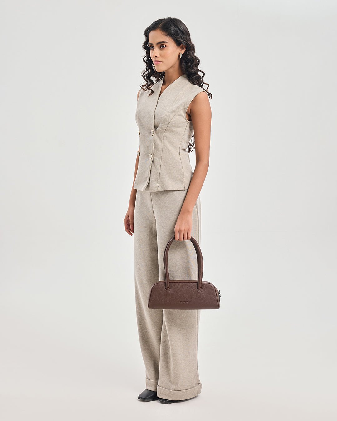 Dark brown top-handle handbag carried by model with short handles and zip front pocket.