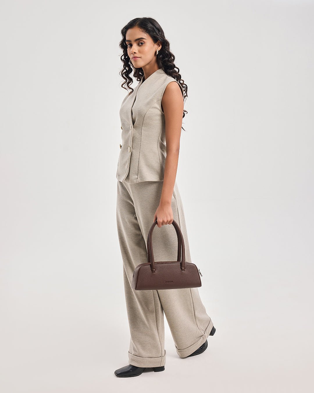 Dark brown top-handle handbag on model’s arm, structured shape with metal zipper pull.