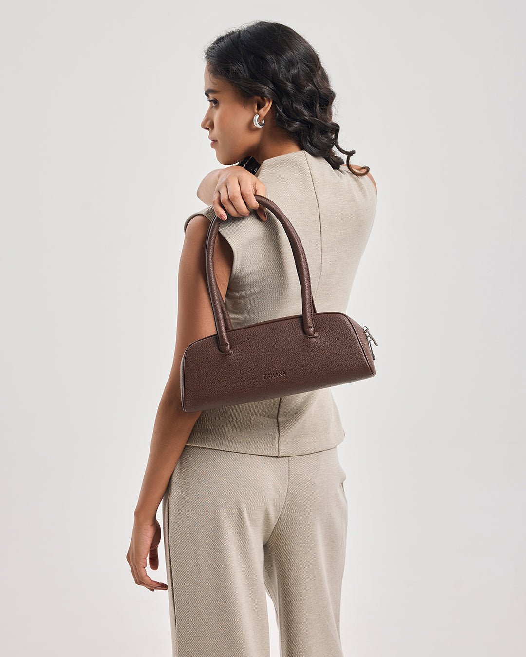 Dark brown handbag worn at side by model, with short handles and small side zipper.
