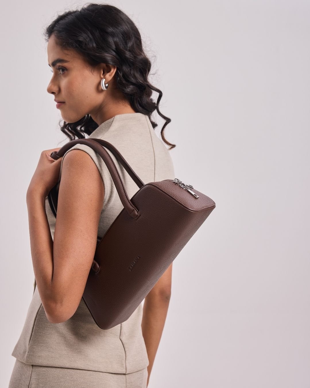 Dark brown top-handle handbag with short handles and zip closure, worn crossbody.