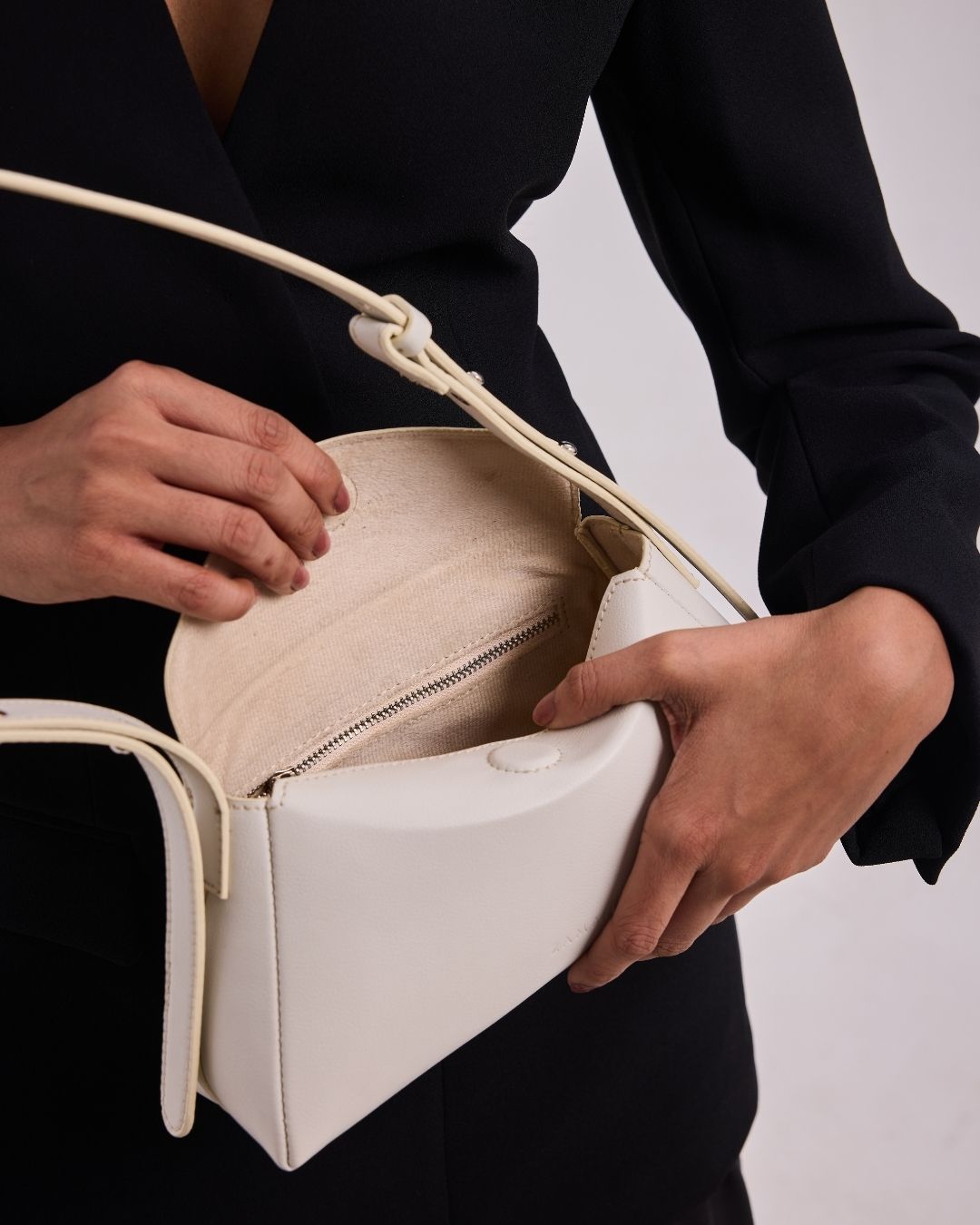 White mini shoulder bag with top handle, zip closure, and rope-style shoulder strap.