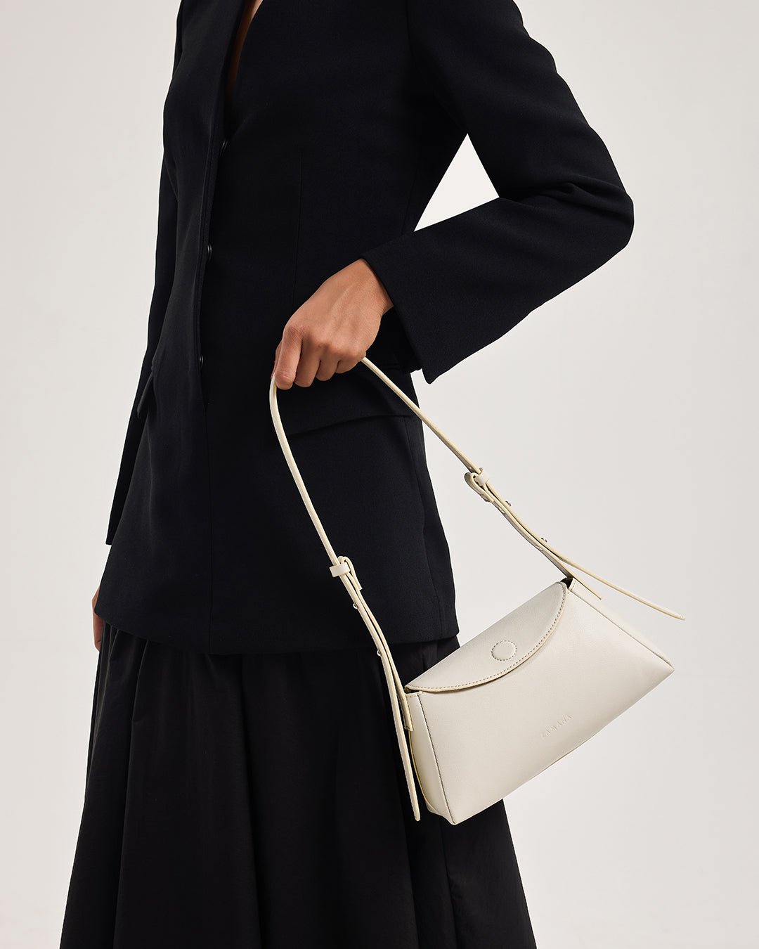 White mini shoulder bag held in hand with rope handles and curved front flap detail.