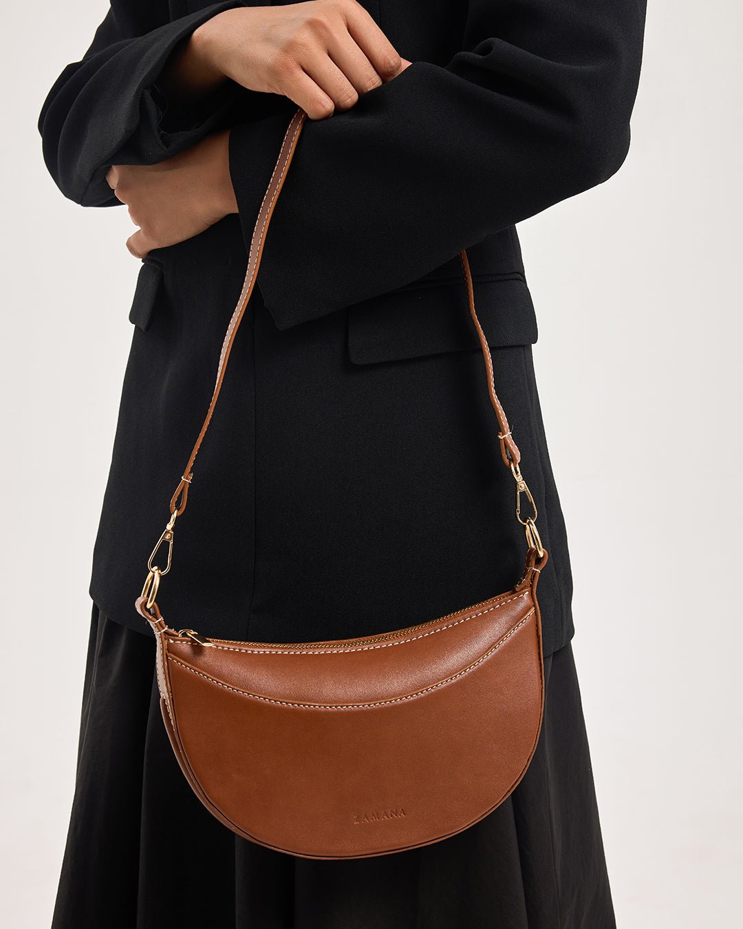 Tan half-moon crossbody bag with chain strap worn at hip