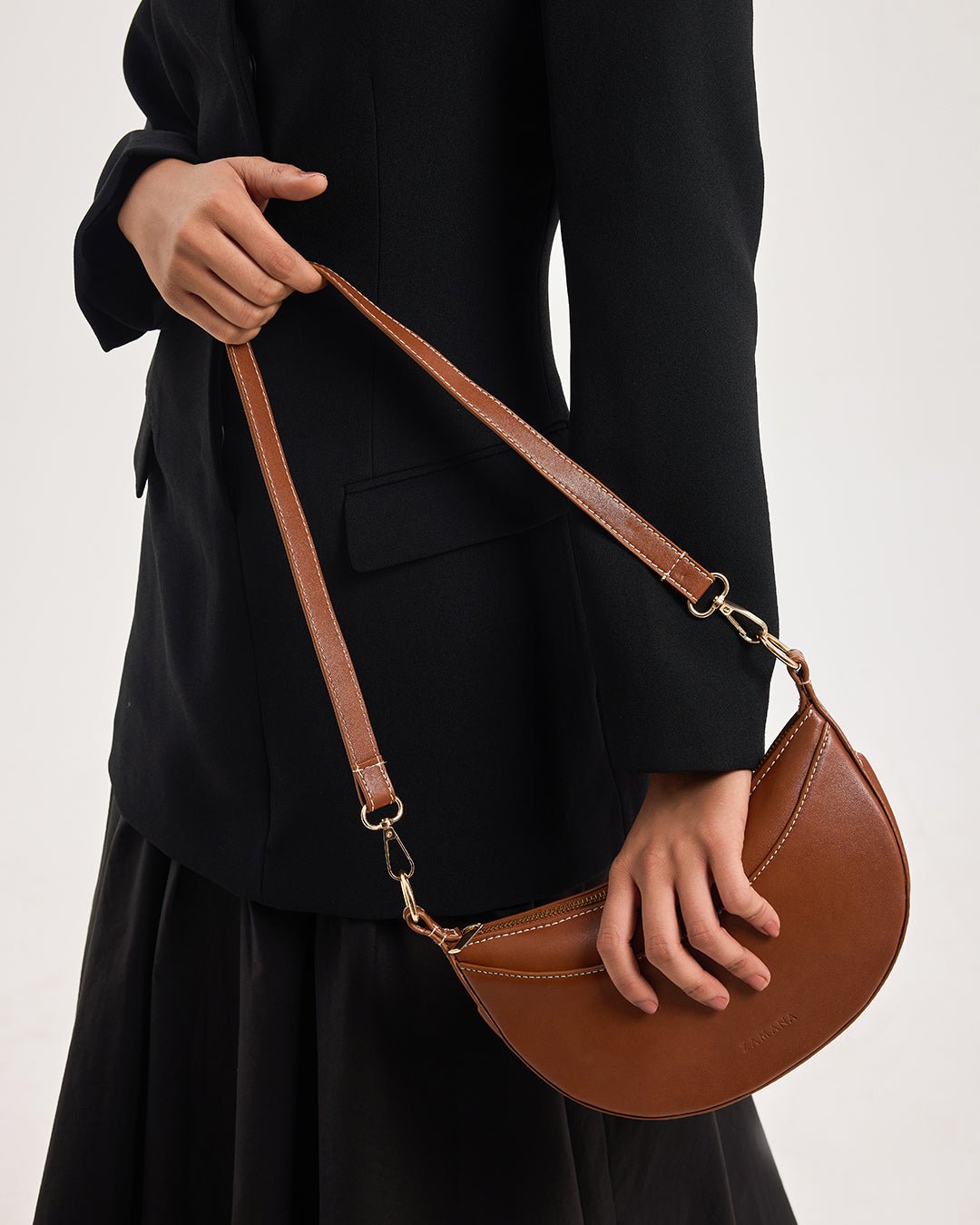 Tan half-moon crossbody bag with long chain strap worn by model