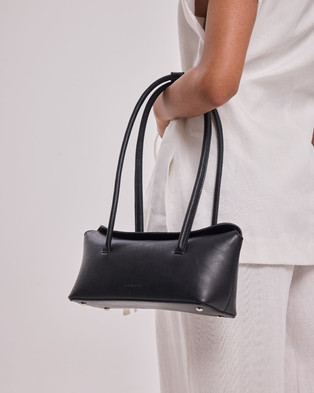 Black structured handbag with two top handles, worn at side