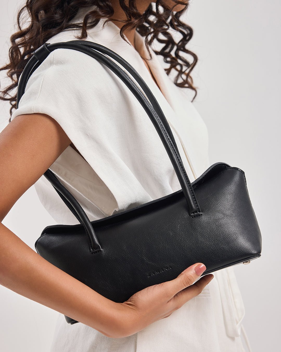 Black handbag with two top handles in the foreground, held by the side