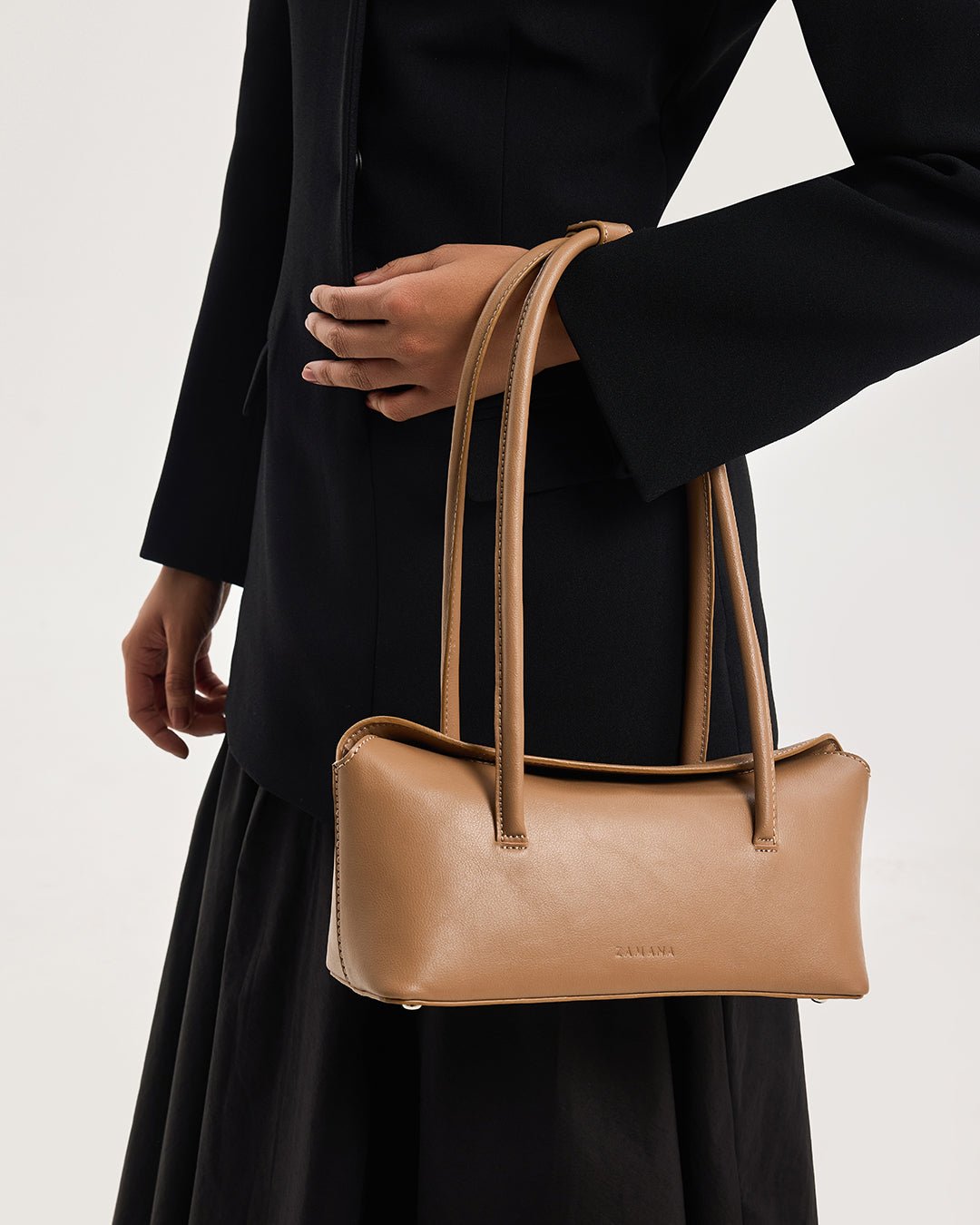 Caramel mini tote bag with top handles and front logo, held by model